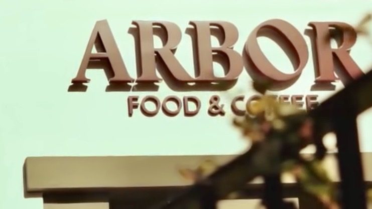 Raised lettering spelling Arbor Food & Coffee on the café wall above its pergola in Funchal