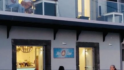 The front of Bar da Lapa in Paúl do Mar after dark, its painted sign between two lit doorways and a guitarist playing on the balcony above