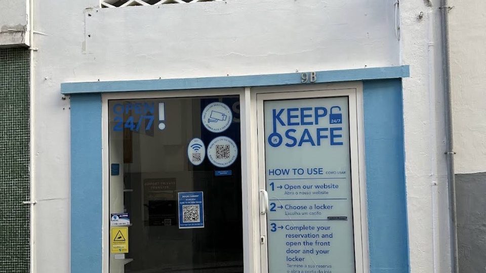 The blue and white shopfront of Keep it Safe 24/7 at Travessa do Freitas 9B in Funchal, with Open 24/7 on the window and the three booking steps printed on the glass door