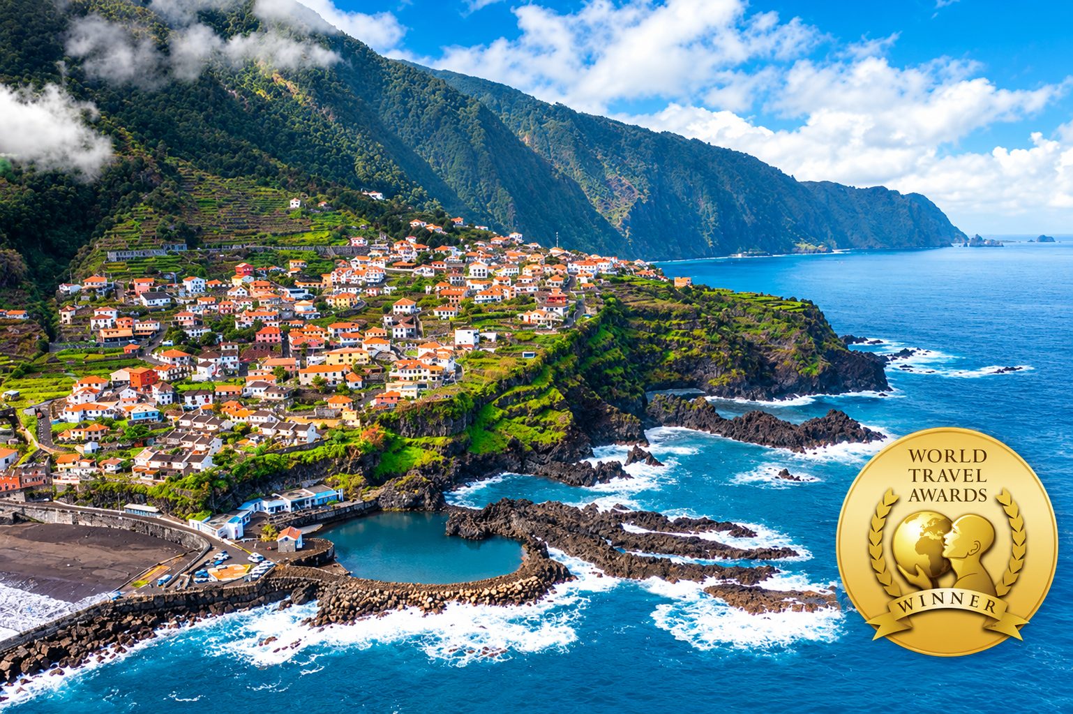A Madeira coastal village of orange rooftops on terraced slopes above a natural sea pool, with the World Travel Awards winner medallion in the corner