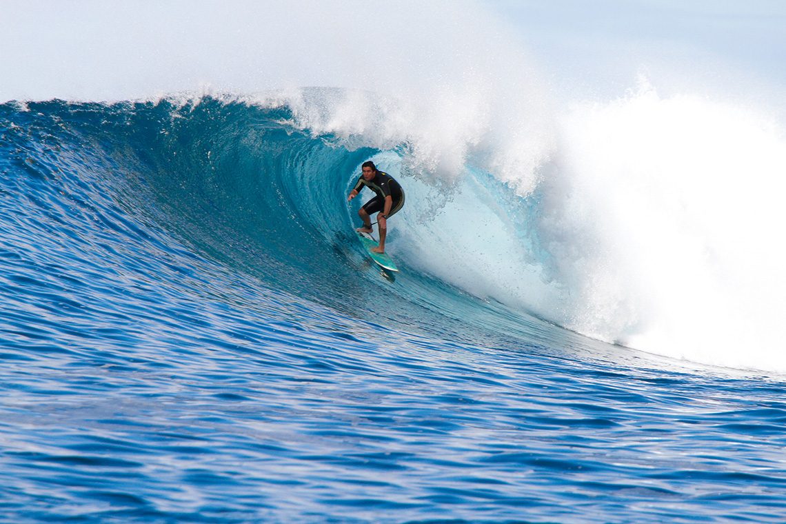 Surfer in a black wetsuit riding deep inside the barrel of a large blue wave