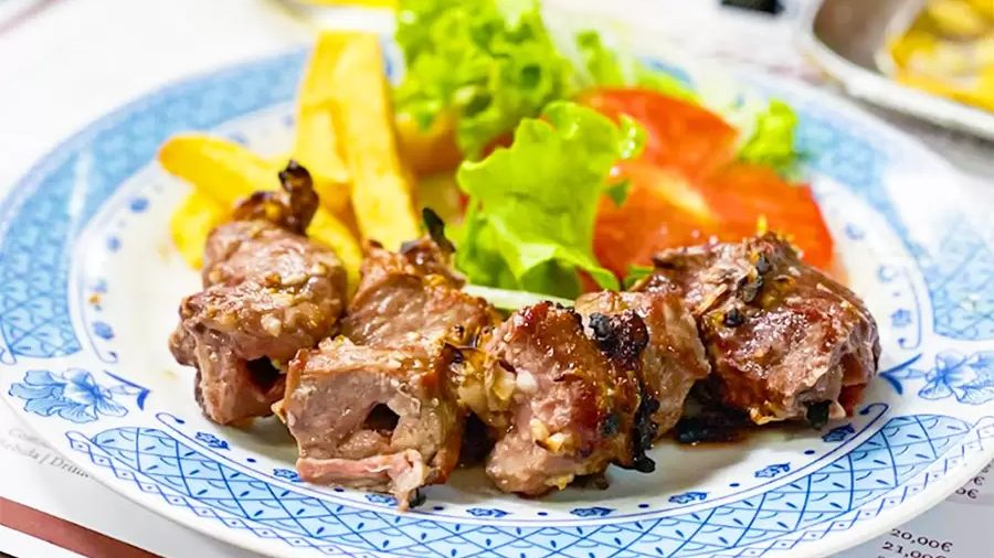 A plate of grilled beef espetada with chips and a lettuce and tomato salad at Restaurante Viola in Estreito de Câmara de Lobos
